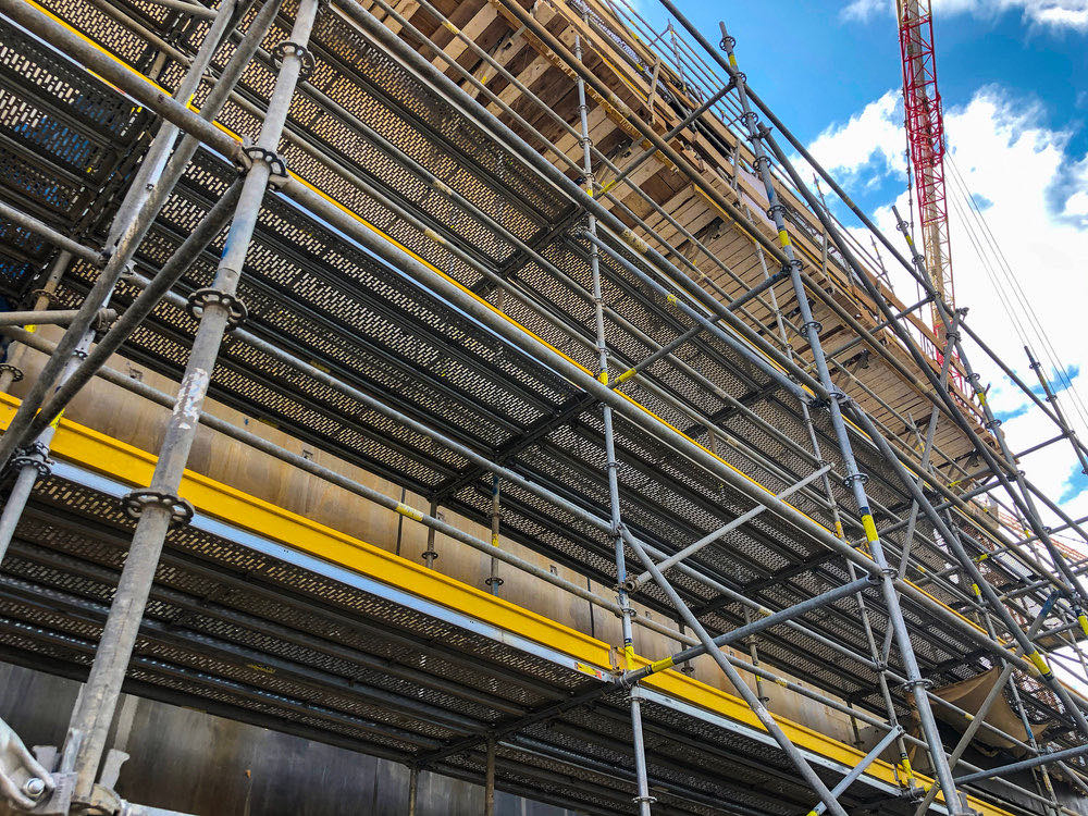 Multi-lift scaffolding across a large commercial construction site with a tower crane overhead